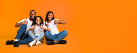 Happy black family gesturing thumbs up sitting on floor, panoramaの写真素材