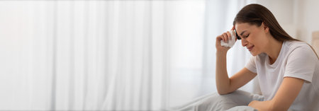 Young woman sitting on a bed, holding her head, feeling stressed at homeの写真素材