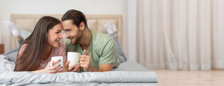 Couple enjoying coffee together while lounging on a cozy bed in a sunny roomの写真素材