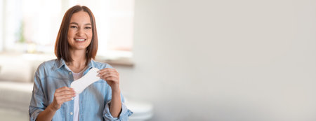 Smiling woman holds a piece of paper in a bright, modern kitchen settingの写真素材