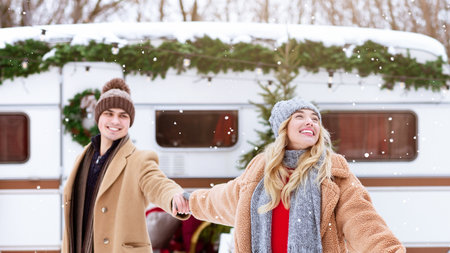 A couple enjoys winter snow while holding hands outside a cozy camper vanの写真素材