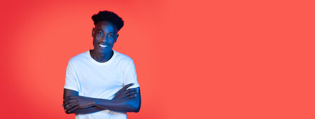 Young man smiling with crossed arms against vibrant orange backgroundの写真素材