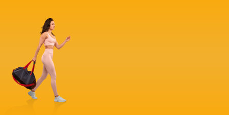 Young woman in activewear with duffel bag on yellow backgroundの写真素材