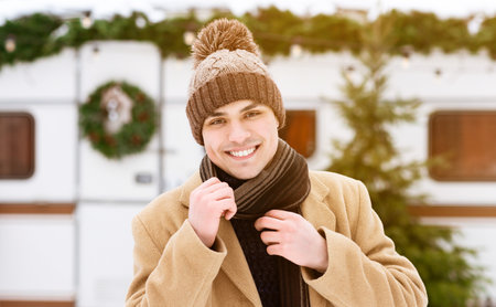 Young man smiles warmly in winter attire near a decorated mobile home in snowの写真素材