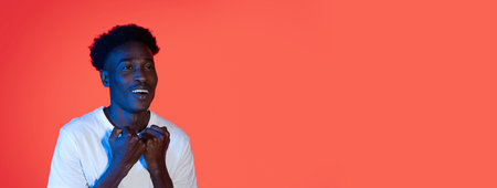 Young man smiling and expressing excitement against a vibrant orange backgroundの写真素材