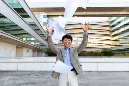 A man is happily throwing papers into the air, expressing excitement outdoorsの写真素材