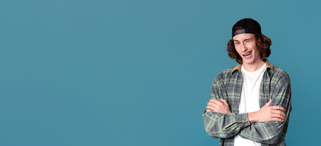 Emotional millenial guy with crossed arms winking on turquise backgroundの写真素材