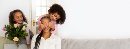 Two daughters surprise their mom with flowers in a cozy living room settingの写真素材