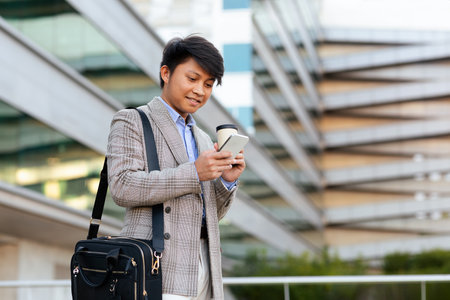 Businessman checks smartphone while walking outside a modern office buildingの写真素材