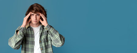 Stress control. Unhappy teenager holding his head with hands on turquoise background