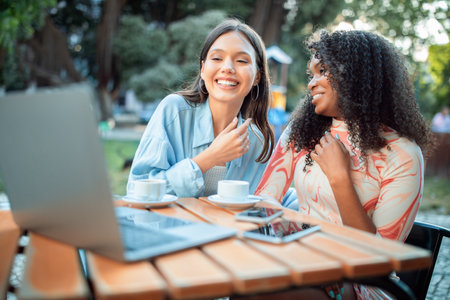 Two friends enjoying coffee and conversation outdoors in a sunny cafe settingの写真素材