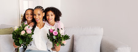 Mother with two daughters holding flower bouquets in a cozy living room settingの写真素材