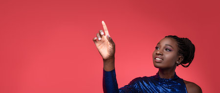 Young woman gestures upward against a vibrant red backdrop in stylish attireの写真素材
