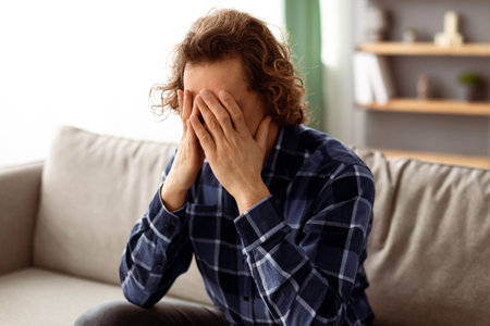Unhappy Guy Covering Face Suffering From Depression Sitting At Homeの写真素材
