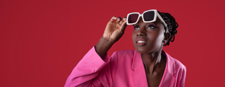 Young woman adjusts stylish sunglasses against a bright red backgroundの写真素材