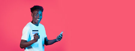 Young man using a smartphone and credit card against a vivid pink background