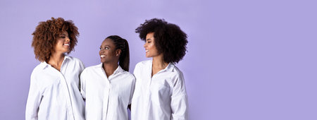 Happy three african american ladies embracing over purple backgroundの写真素材