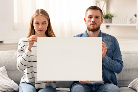 Young married couple holding blank poster at homeの写真素材