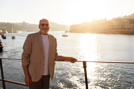 Man in light jacket enjoying sunset by the waterfront in a bustling harborの写真素材