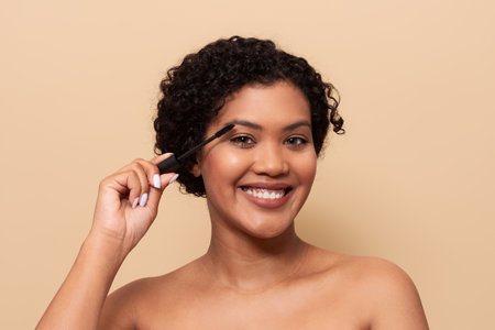 A woman applying mascara while smiling in a beauty routine at home