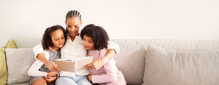 A mother reads a storybook to her daughters on a cozy sofa at homeの写真素材