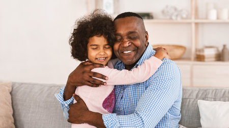 Stay at home, be happy. African American grandpa hugging his lovely granddaughter in light roomの写真素材