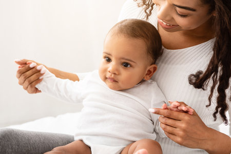 African Mom Cuddling Playing With Adorable Little Baby In Bedroom