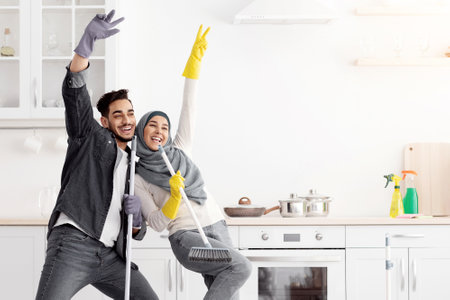 Funny muslim couple singing songs while cleaning kitchen, copy spaceの写真素材