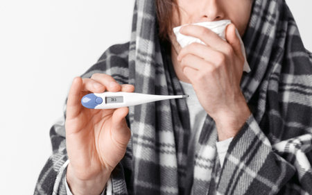 Fever and illness. Man coughs, covers his mouth with napkin and shows thermometer with high...