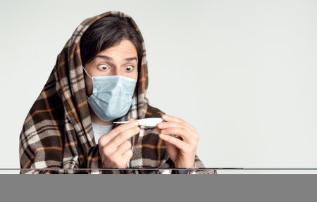 Man in protective mask looks at thermometerの写真素材