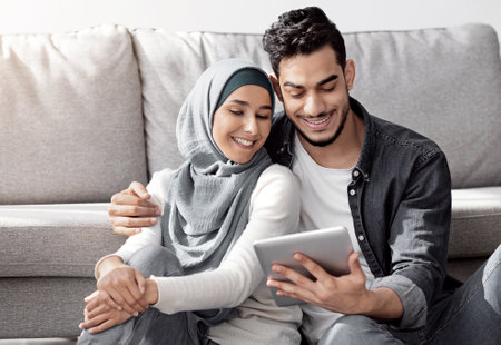 Loving muslim family sitting on floor with tablet among boxesの写真素材