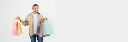 Cheerful senior man holding colorful shopping bags in two handsの写真素材