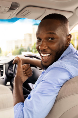 Happy black man sitting in car showing thumbs up gesture