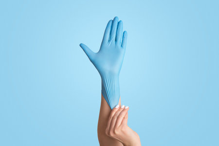 Infectious disease protection. Young female putting on blue medical glove against white background, closeupの写真素材