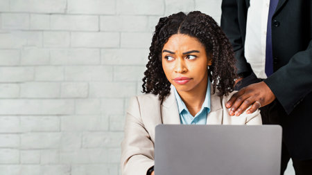 Sexual misconduct at workplace. African American boss touching his female subordinates shoulder in officeの写真素材
