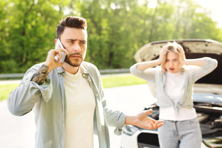Young guy standing near broken car together with terrified girlfriend, having auto accident, calling...