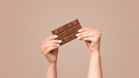 Unrecognizable millennial girl holding bar of chocolate on pink background, copy spaceの写真素材