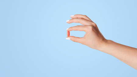 Closeup of female hand holding red pill on white backgroundの写真素材