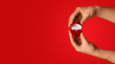 Male hands holding box with beautiful engagement ring on orange background, empty space. Panoramaの写真素材