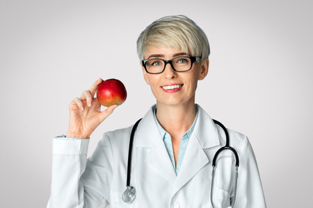 Healthy eating concept. Adult woman doctor in glasses holds red apple in handの写真素材