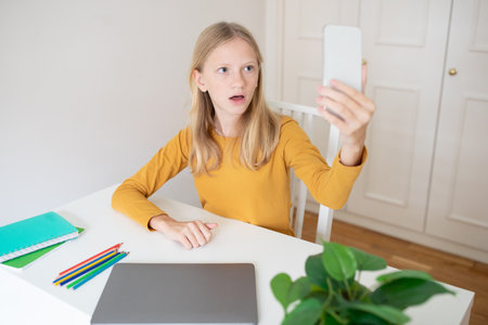 European teenage girl engaged in face timing with friends at homeの写真素材