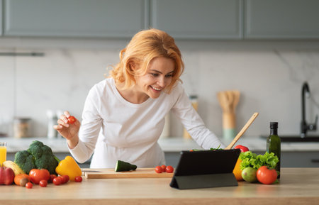 A woman with blonde hair is smiling as she cooks in a contemporary kitchenの写真素材