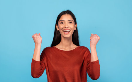 Joyful millennial woman celebrating success against a blue backdropの写真素材
