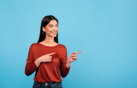 Brunette woman smiling and gesturing on a blue backgroundの写真素材