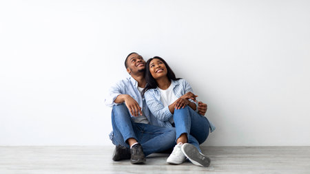 Decoration and furniture concept. Happy african american couple sitting on floor in new appartment, planning interiorの写真素材