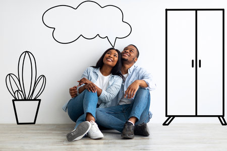 Dreaming african american spouses imagining interior of their new flat, sitting on floor near wall with doodle drawingsの写真素材
