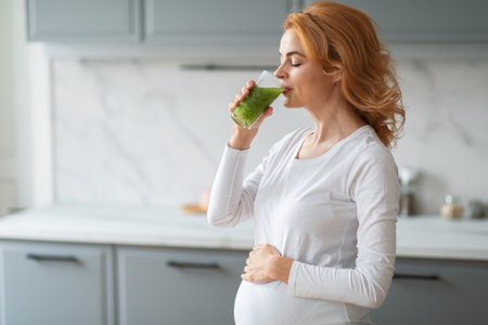 Pregnant woman enjoying green smoothie in modern kitchen during morning