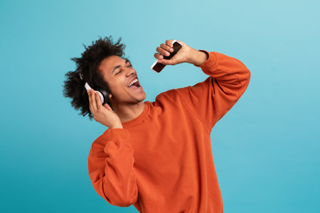 Young man with curly hair enjoys music and sings passionately with headphones