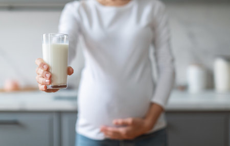 Pregnant woman holding glass of milk in modern kitchen during morningの写真素材