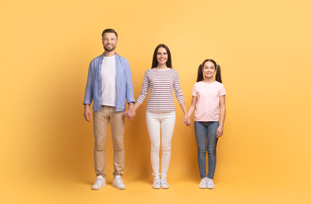 Family of three stands together against a vibrant yellow backgroundの写真素材